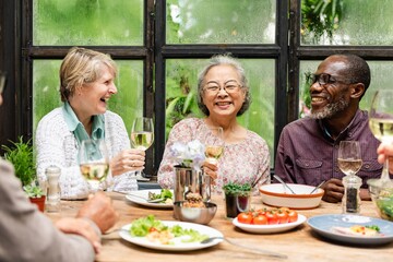 Group of diverse senior friends celebrate at restaurant. Happy senior friends celebrate with wine...
