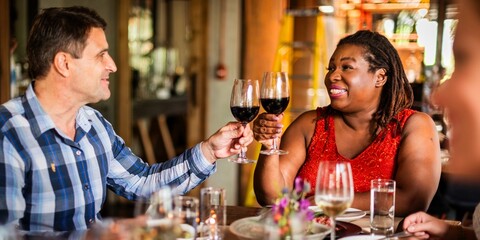 A diverse group enjoying a meal, toasting with wine glasses. Smiling, happy, diverse friends dining together, sharing a joyful moment over drinks and food. Friends celebrating at dinner party.