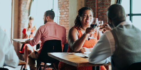 Diverse people dining in a cozy fancy restaurant. Two couples enjoy wine and conversation. Warm lighting and brick walls create a relaxed dining atmosphere.