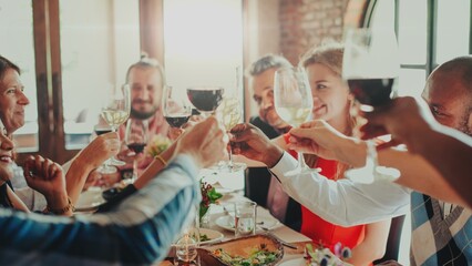 Group of people toasting with wine glasses at a dining table. Celebration with friends, diverse group enjoying a meal together, raising glasses in a toast. Celebrations, Communal dining.