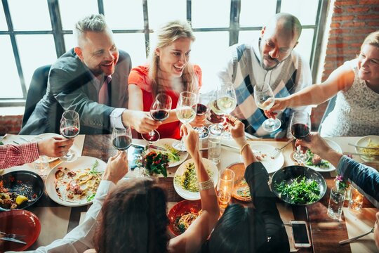 Group of diverse people enjoying a meal, toasting with wine glasses. Celebration, food, and friends gathered around a table, sharing joy and laughter. Celebrations, Communal dining, festive season.