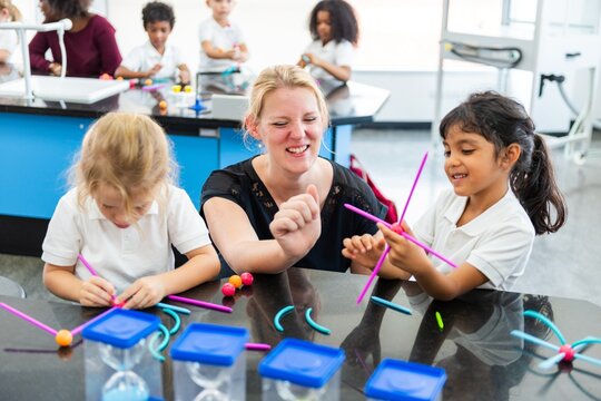 Teacher with diverse children in a classroom, in a STEM activity. Kids and teacher enjoying STEM learning with colorful materials in a lively classroom. Teacher working with elementary school children
