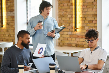 Three colleagues share ideas in a trendy workspace, actively collaborating over coffee and devices