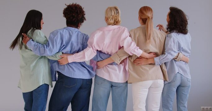 Back view portrait of a group of diverse women friends wearing casual clothes hugging each other and dancing on grey wall background. Diversity, people and friendship concept. 4k video. Slow motion.
