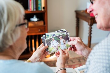 Elderly couple looking at old photos, reminiscing. The couple enjoys memories, sharing stories. Photos bring nostalgia and connection to the elderly pair. Elderly couple looking at photos at care home