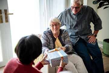 Elderly couple receiving a gift from an Indian woman. Smiling elderly woman and man got a gift. Gift exchange between elderly people in retirement home. Happy elderly moment with a present.