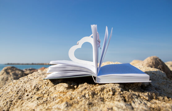 An open book on the beach on a sunny day. A wooden heart as a bookmark. Digital detox, book lovers on vacation
