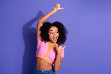 Obraz premium Cheerful young woman in casual wear smiling and pointing with excitement against a vibrant purple background