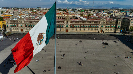 Aerial view of Mexican flag waving in the foreground, National Palace and Popocatepetl volcano in the background at the Zocalo in Mexico City