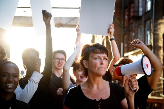 Woman with megaphone in diverse group of people holding protest signs. Group of various ethnicity people united in protest. Woman with megaphone with diverse people in protest with blank paper signs