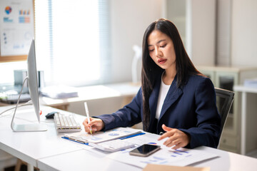 A woman is sitting at a desk with a computer monitor and a notebook