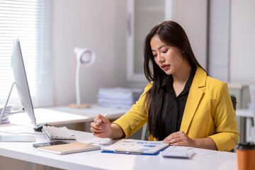 A woman in a yellow jacket is sitting at a desk with a computer monitor