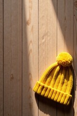 A Sunny Yellow Knitted Winter Hat with Pompom Resting on Light Wooden Planks