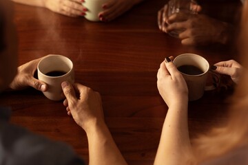 A group of people enjoying coffee together. Hands holding coffee cups. Coffee cups on wooden table. Coffee time with friends. Diverse group sharing coffee moments. Diverse group of people with coffee