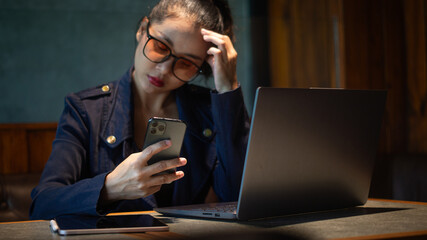 Businesswoman stressed out at work and tracking investment prices on smartphone in hand with laptop and tablet on desk.