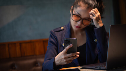 Businesswoman scratching her head in confusion due to stress from work and tracking investment prices on smartphone in hand with laptop and tablet on desk, blank space for text.