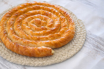 Traditional spiral borek on woven placemat Freshly baked spiral borek. Savory pastry made with flaky phyllo dough. Selective focus.