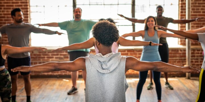 Group exercise class with diverse participants stretching arms. Mixed gender and ethnicity. Fitness and stretching in a bright studio. Diverse people in gym class.