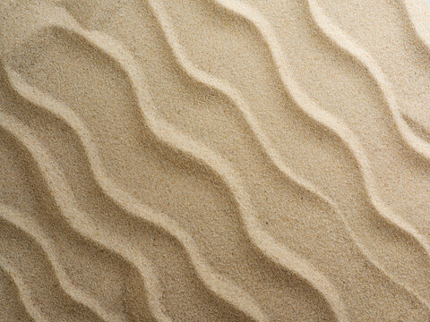 Beach sand background with natural wave pattern. Summer background of beach sand with small stones along the edges. Tourism, vacation and holidays concept. Top view.