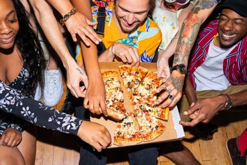 Group of diverse friends eagerly reaching for pizza, sharing laughter and joy. Multiracial friends...