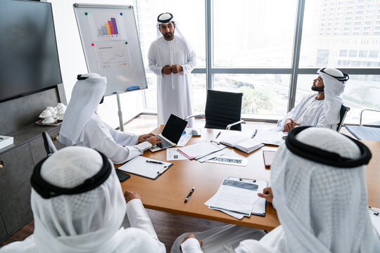 Arab businessmen wearing emirati kandura meeting in office for business deal - Corporate business group of middle-eastern people working in an international company in middle east - Powered by Adobe
