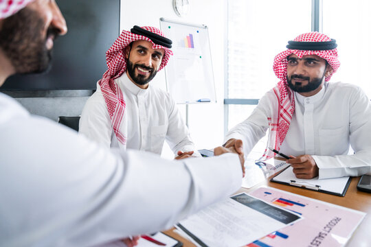 Arab businessmen wearing saudi kandura meeting in office for business deal - Corporate business group of middle-eastern people working in an international company in middle east