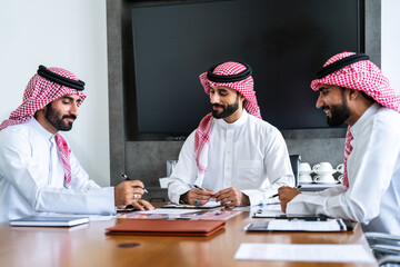Arab businessmen wearing emirati and saudi kandura meeting in office for business deal - Corporate business group of middle-eastern people working in an international company in middle east