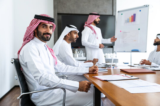 Arab businessmen wearing emirati and saudi kandura meeting in office for business deal - Corporate business group of middle-eastern people working in an international company in middle east