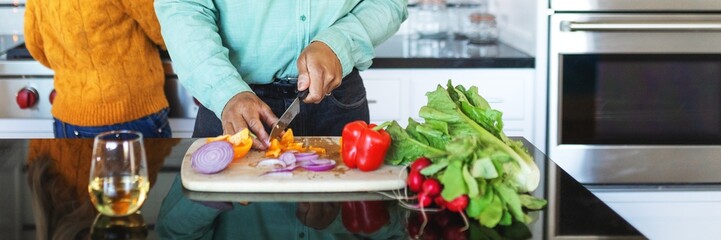 Man chops vegetables in modern kitchen preparing meal. Man cooking in kitchen with fresh ingredients. Couple preparing healthy food in the kitchen. Man preparing food by chopping vegetable at counter