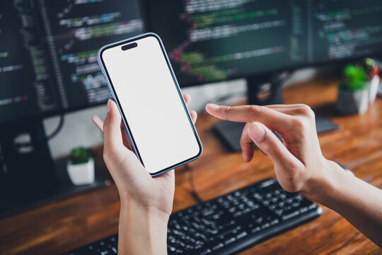 Young female software developer using smartphone for coding in modern workspace with computer screens and programming tools