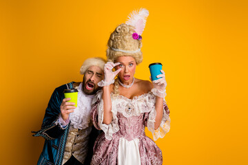 Elegant couple in royal costumes with coffee cups on a vibrant yellow background, showcasing historic style and a modern twist with humor.