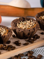Brown muffins on wooden tray among coffee beans on striped fabric, close-up, vertical image.