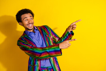 Charismatic young man wearing a bold, colorful jacket poses cheerfully on a vibrant yellow...