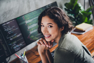 Smiling young female programmer working in home office with computer screens displaying coding...