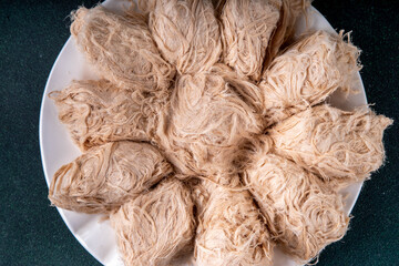 Traditional Asian sweets Pishmaniye, also known as Pashmak, Dragon's Beard, or Kkul Tarae, thread-like hair halvah, with nutty flavor, on a plate, copy space