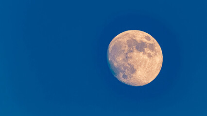 Detailed megazoom (600mm) winter view of the moon with craters during daytime with blue sky