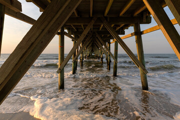 Beneath the Oak Island fishing pier in North Carolina as ocean waves crash onto the shore at...