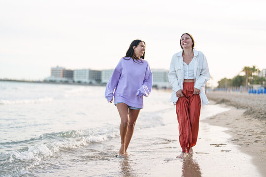 Two Female Friends Walking Happily on a Sandy Beach at Sunset in Relaxed Casual Outfits