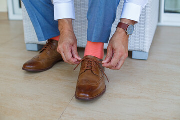 close up of brown shoes.man tying his brown leather dress shoes, featuring a smart, formal look with a white shirt, a light blue suit, and vibrant coral socks. groom at the wedding