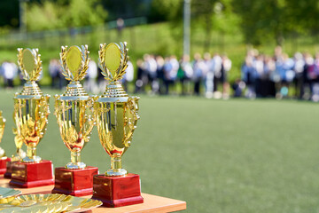 Award cups rest on a table with a blurred crowd behind, capturing the excitement and triumph of a...