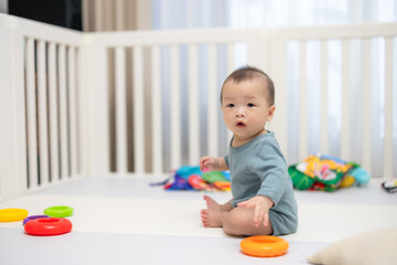 Adorable baby sitting in white crib playing with toys