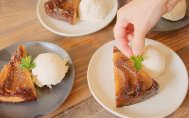 Homemade apple upside-down cake served with vanilla ice cream, garnished with fresh mint on a wooden table in warm ambient light.