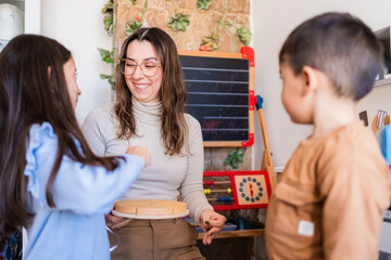 Smiling teacher holding fraction circle board playing with children in montessori classroom