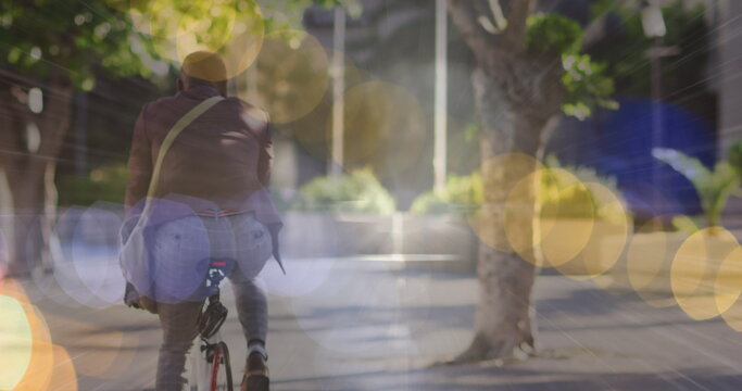 Image of glowing lights over african american businessman cycling in city