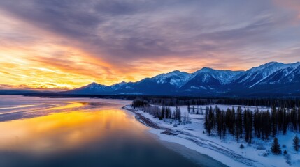 Obraz premium Serene winter sunset over a tranquil lake with snow-covered mountains in the background