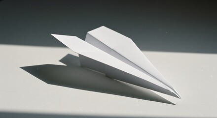 Simple white paper airplane resting, casting a stark shadow on a bright surface
