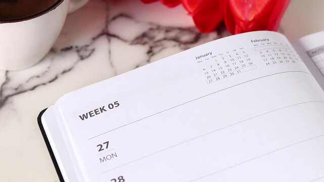 Flipping week calendar notebook pages with coffee cup and red tulips. Annual goals, new year budget, aspirations, monthly schedule concept.