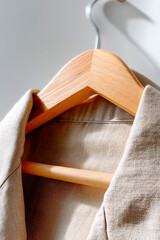 Close-up of beige linen shirt on a wooden hanger with soft daylight highlighting the fabric texture and minimalist design
