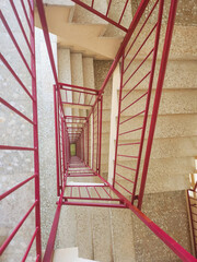 Abstract top-down view of a stairwell with red railings, forming a symmetrical spiral pattern. Urban geometry.