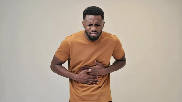 Adult man grimacing in discomfort, clutching stomach with both hands due to possible abdominal pain
